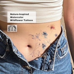 May include: A watercolour wildflower tattoo design featuring delicate blue and pink flowers with stems and leaves. The tattoo is applied to a person's lower abdomen. The text "Nature-Inspired Watercolor Wildflower Tattoos" and "The Old Story" is visible in the image.