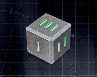 May include: A gray, textured, cube-shaped die featuring recessed, bright neon green slots representing numerical values. The top face displays three vertical slots, while the front and side faces show one and two slots respectively.