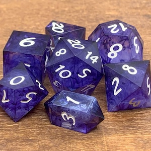 May include: Set of seven polyhedral dice in shades of purple with white numbering. The dice are made of a translucent material with a swirling pattern. The dice are for tabletop games like Dungeons and Dragons.