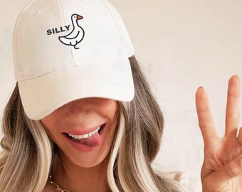 May include: White baseball cap with the word "SILLY" above a cartoon goose illustration. The cap is made of a soft material and has a curved brim. The cap is a casual accessory.