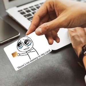 K&ouml;nnte beinhalten: Eine wei&szlig;e rechteckige Kreditkarte mit einer schwarz-wei&szlig;en Strichzeichnung einer weinenden Strichm&auml;nnchen-Figur, die einen goldenen EMV-Chip h&auml;lt. Der aufgedruckte Text lautet, There's no money in my card. Die Karte hat einen goldenen Zahlungs-Chip.