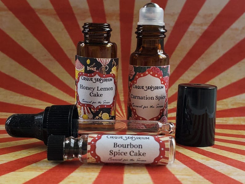 May include: Three glass bottles with rollerball tops and labels that read "CIRQUE SENSORIUM" and feature different scents: "Honey Lemon Cake", "Carnation Spice", and "Bourbon Spice Cake".
