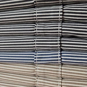 May include: Close-up of a stack of folded fabric with horizontal stripes in various colors. The stripes include black and white, navy and white, and tan and white. The fabric is neatly folded and stitched.