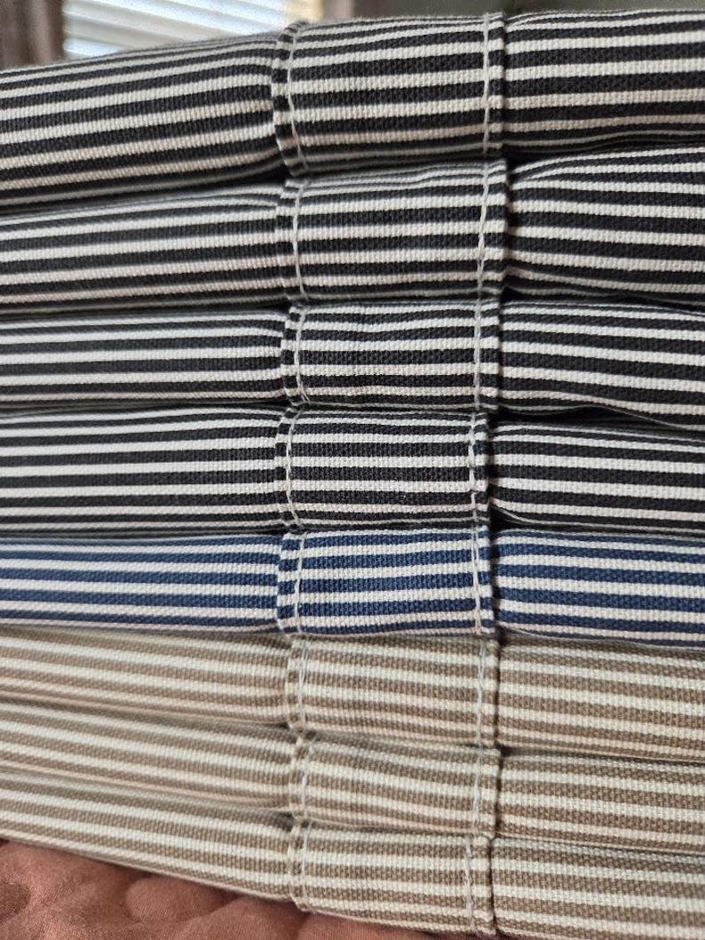 May include: Close-up of a stack of folded fabric with horizontal stripes in various colors. The stripes include black and white, navy and white, and tan and white. The fabric is neatly folded and stitched.