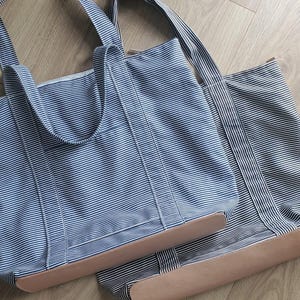 May include: Two blue and white striped tote bags with tan leather bottoms. The bags have matching blue and white striped handles. The bags are made of a sturdy fabric and are designed for carrying items.