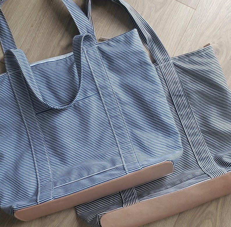 May include: Two blue and white striped tote bags with tan leather bottoms. The bags have matching blue and white striped handles. The bags are made of a sturdy fabric and are designed for carrying items.