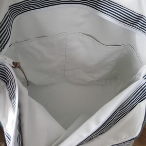 May include: White tote bag with navy blue stripes. The bag has a large interior with a zippered pocket and a small leather accent. The exterior features a striped pattern, and the interior is a solid white color.