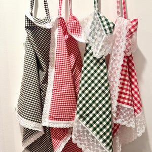 May include: Three gingham tea towels with white lace trim. The towels are black and white, red and white, and green and white.