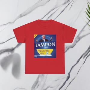May include: Red t-shirt with a graphic of a blue and yellow box that says "Tampon Tim" with a picture of a man in a suit and tie. The box also says "New" and "40 Regular/Super" and "Make America Flow Again".