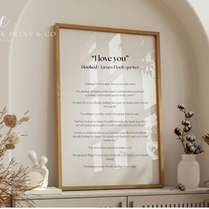 Puede incluir: Una impresi&oacute;n enmarcada con el texto "I love you" y citas de James Hook. La impresi&oacute;n est&aacute; en un marco de madera clara y se exhibe en un estante blanco con elementos decorativos, incluyendo plantas secas y una peque&ntilde;a escultura blanca.