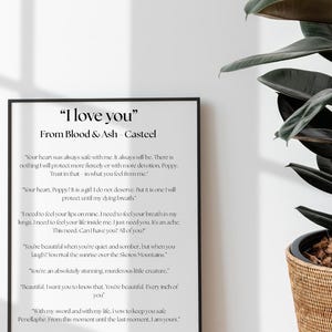 May include: A framed print with the text "I love you" from Blood & Ash - Casteel. The black framed print is displayed against a white wall, with a large green plant in a woven basket to the right.