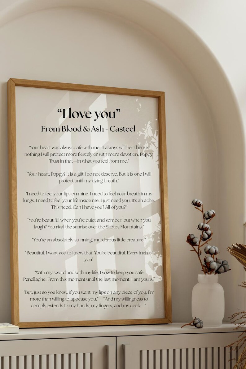 May include: A framed print with the text "I love you" from Blood & Ash - Casteel. The print has a light wood frame and features romantic quotes. A white vase with cotton stems sits to the right.