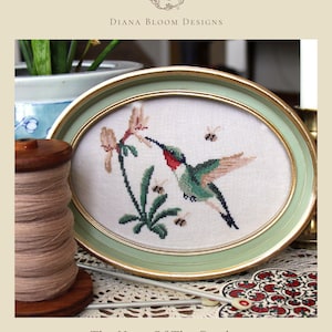 Puede incluir: Un diseño de punto de cruz enmarcado ovalado con un colibrí y flores, con un marco verde y dorado. El texto "The Hum Of The Garden" está en la parte inferior. El diseño está sobre un fondo blanco. El nombre del diseñador está en la parte superior.