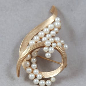 May include: A gold tone brooch with a swirling design and a cluster of faux pearls.