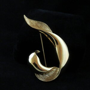 Puede incluir: Un broche dorado en forma de hoja estilizada, con un diseño liso y curvo.