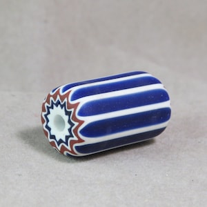 Puede incluir: Una cuenta de vidrio rayada azul y blanca con un diseño de estrella roja y blanca en un extremo.