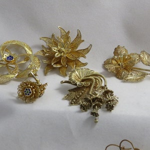 Puede incluir: Cinco broches de filigrana dorada con intrincados diseños florales. Las broches presentan una variedad de formas, incluyendo una flor, una estrella y un círculo. Las broches están hechas de oro y tienen un diseño delicado e intrincado.
