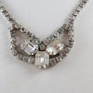 Puede incluir: Un collar de plata con una cadena delicada y un grupo de tres piedras transparentes y facetadas en el centro.