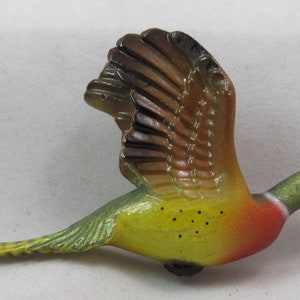 Puede incluir: Una figurita de cerámica de un faisán en vuelo. El faisán está pintado en tonos de verde, amarillo, rojo y marrón. Las alas están extendidas y las plumas de la cola están extendidas.