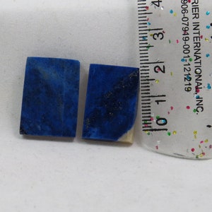 Puede incluir: Dos piezas rectangulares de lapislázuli, una piedra preciosa azul oscuro con motas de pirita dorada, se muestran junto a una regla. Las piezas miden aproximadamente 2,5 cm de largo.