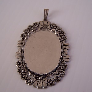 Puede incluir: Pendiente plateado con diseño floral. El pendiente tiene un espacio ovalado en blanco en el centro para agregar un camafeo u otro adorno.