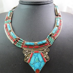 Puede incluir: Un collar de múltiples hilos con cuentas de turquesa y coral, un colgante de plata con una piedra de turquesa grande y una cadena de plata.