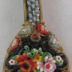 Puede incluir: Un broche vintage de mosaico con forma de mandolina con un diseño floral. El broche está hecho de pequeñas baldosas de vidrio en tonos de rojo, verde, blanco, negro y azul.