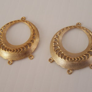May include: Two gold-tone metal earring findings with a decorative, openwork design. Each finding has three jump rings.