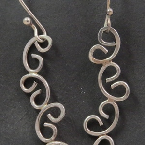 Puede incluir: Un par de pendientes de plata con un diseño delicado y en espiral. Los pendientes están hechos de alambre fino y retorcido y tienen un cierre de gancho simple.