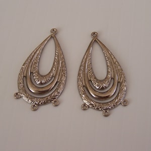 Puede incluir: Un par de hallazgos de pendientes de metal plateado en forma de lágrima con tres bucles en la parte inferior. La forma de la lágrima tiene un diseño intrincado con tres círculos concéntricos.