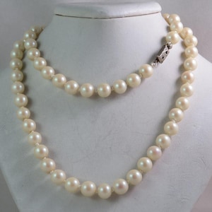 Puede incluir: Un collar de perlas clásico con un cierre de plata. Las perlas son blancas y redondas, y el collar está enhebrado en una fina cadena de plata.