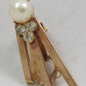 Puede incluir: Pendientes de clip de tono dorado con una sola perla falsa y tres diamantes de imitación transparentes.