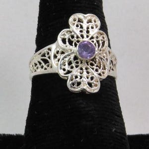 Puede incluir: Un anillo de filigrana de plata con una piedra preciosa púrpura en el centro.
