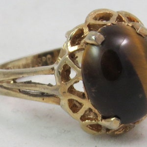 Puede incluir: Un anillo de oro con una gran piedra de ojo de tigre ovalada engastada en un delicado diseño calado.
