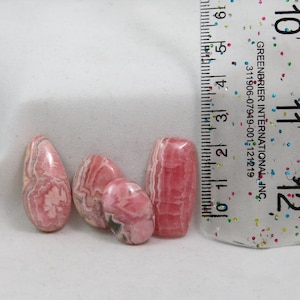 Puede incluir: Cuatro piedras preciosas cabujón pulidas, rayadas de rosa y blanco, con una regla para referencia de tamaño. La regla muestra medidas en pulgadas.