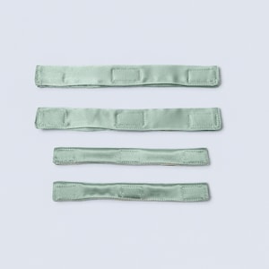 May include: Four sage green satin fabric strips arranged horizontally. Each strip features three rectangular stitched sections along its length, creating a uniform appearance. The material has a smooth, reflective finish consistent with satin fabric.