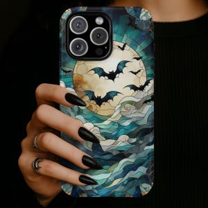 May include: A phone case featuring a stained-glass design with a full moon, bats, and ocean waves in shades of blue, teal, and gold. The case has a glossy finish and a dark border.