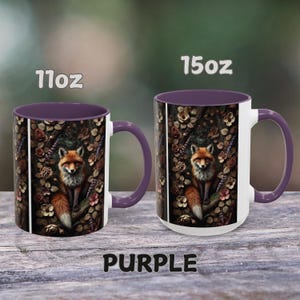 Op de afbeelding: Twee keramische mokken in paars en wit met een vos-illustratie. De mokken zijn verkrijgbaar in de maten 11 oz en 15 oz. De vos is omringd door bloemen en bladeren in een bosrijke omgeving.