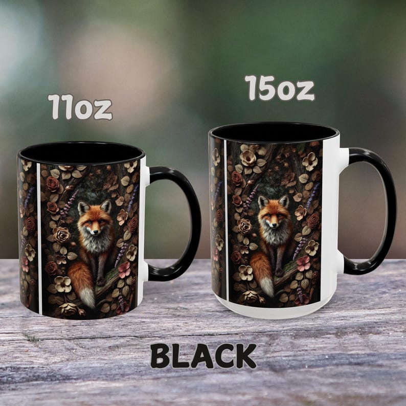 Op de afbeelding: Twee zwarte en witte keramische mokken met een vos-illustratie. De mokken zijn verkrijgbaar in de maten 11 oz en 15 oz. De vos is omringd door bloemen en bladeren. De tekst "BLACK" is onder de mokken gedrukt.