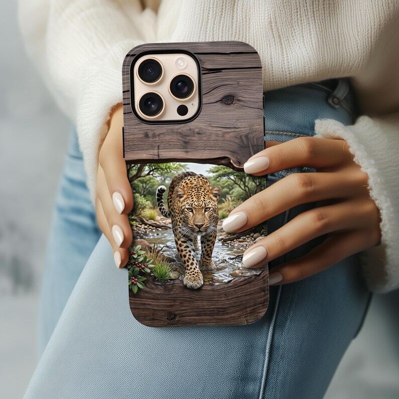 May include: A rectangular smartphone case featuring a dark brown wood grain texture on the top and bottom sections. The center displays a detailed, full-color graphic of a leopard walking through a shallow stream in a lush, green forest setting.