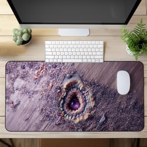 May include: A purple and gray mouse pad with a detailed design of a seashell with a purple gemstone in the center. The mouse pad is on a wooden desk with a computer keyboard and a potted plant.