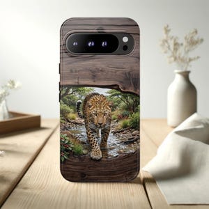 May include: A rectangular smartphone case featuring a printed design of a leopard walking through a shallow stream. The background of the print shows a natural landscape with trees and foliage, framed by a dark brown wood grain texture at the top and bottom.