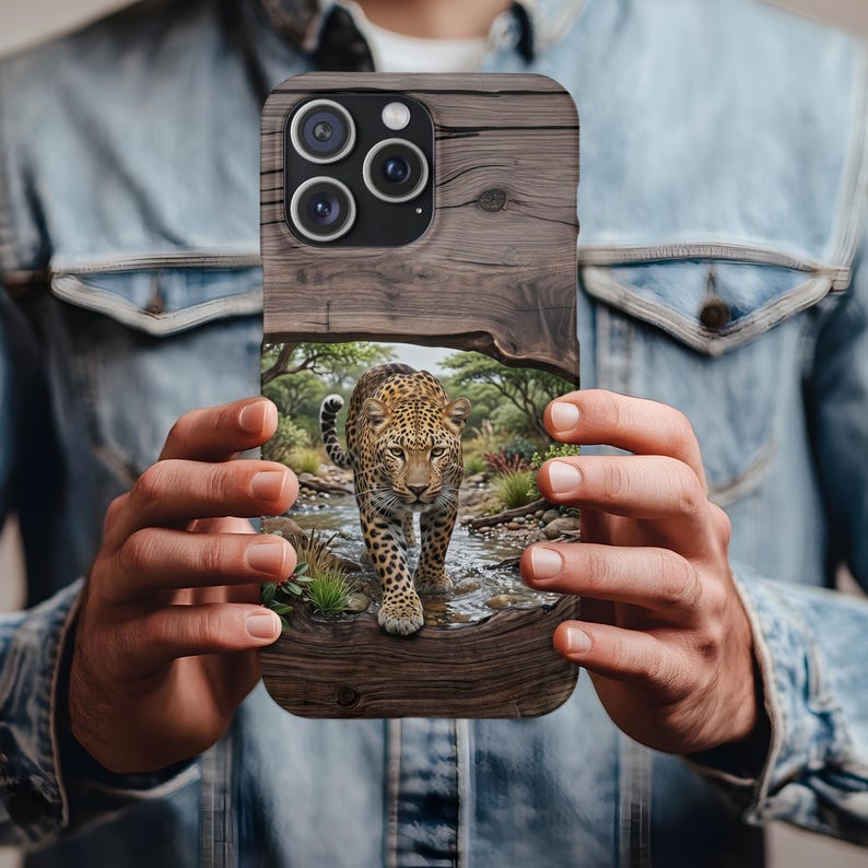May include: A rectangular smartphone case featuring a wood grain texture on the top and bottom sections. The center displays a detailed graphic of a leopard walking through a shallow stream in a grassy, wooded environment with green foliage.