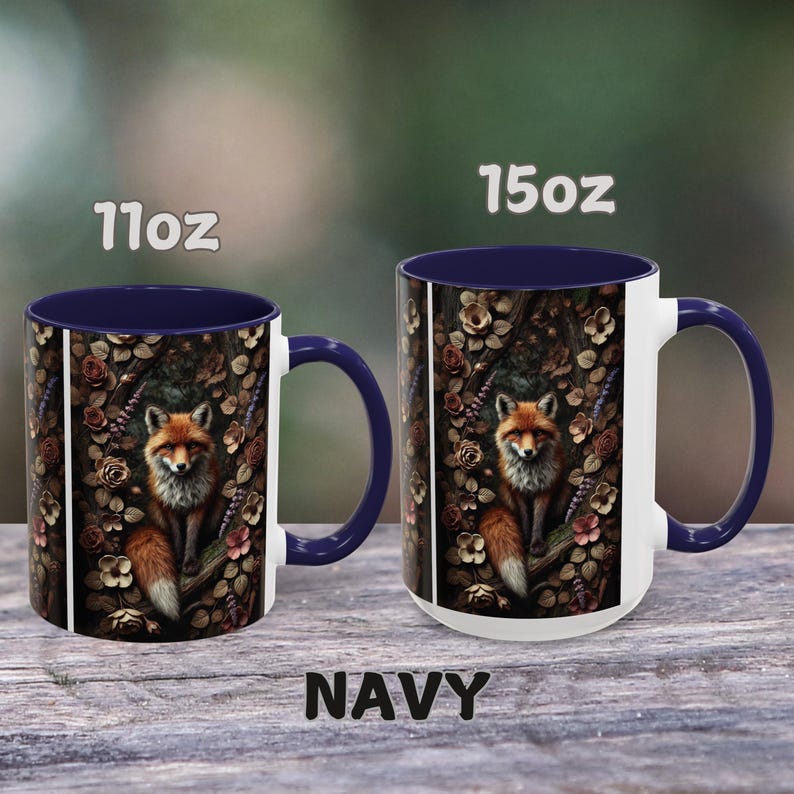 Op de afbeelding: Twee keramische mokken met een marineblauwe rand en handvat. De mokken hebben een witte achtergrond met een kleurrijke illustratie van een vos in een bosomgeving. De tekst "11oz" en "15oz" is op de mokken gedrukt. De tekst "NAVY" is onder de mokken gedrukt.
