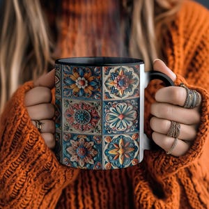 May include: A black and white ceramic mug with a colourful tile pattern featuring floral designs. The mug is filled with a steaming beverage.