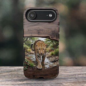 May include: A rectangular smartphone case featuring a dark brown wood grain texture on the top and bottom. The center displays a detailed illustration of a leopard walking through a shallow stream in a savanna landscape with green trees.