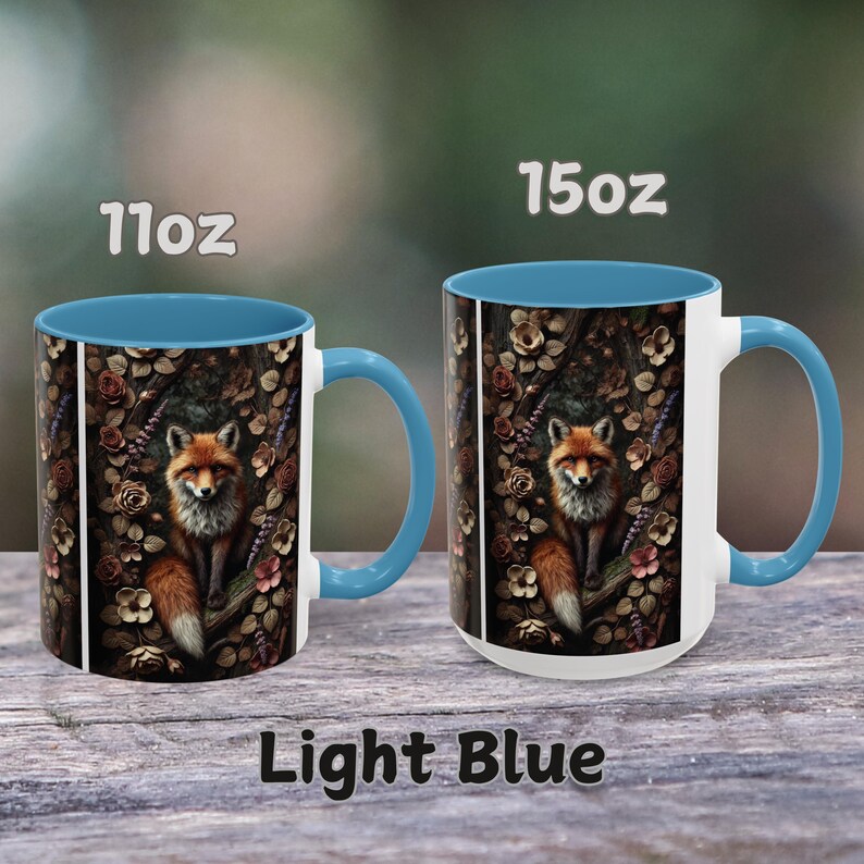 Op de afbeelding: Twee keramische koffiemokken met een lichtblauwe rand en handvat. De mokken hebben een vos-illustratie met een bosachtergrond. De mokken zijn verkrijgbaar in de maten 11oz en 15oz. De tekst "Light Blue" is onder de mokken gedrukt.