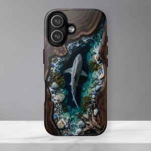 May include: A rectangular phone case featuring a high-resolution graphic of a shark swimming in a deep blue pool of water surrounded by dark wood grain textures, smooth river stones, and small patches of green aquatic vegetation.