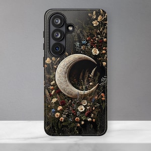 May include: A black smartphone case featuring a detailed silver crescent moon centered amidst a dark, dense arrangement of colorful flowers including red, white, and yellow blossoms. The case has a textured mesh pattern and three camera cutouts.