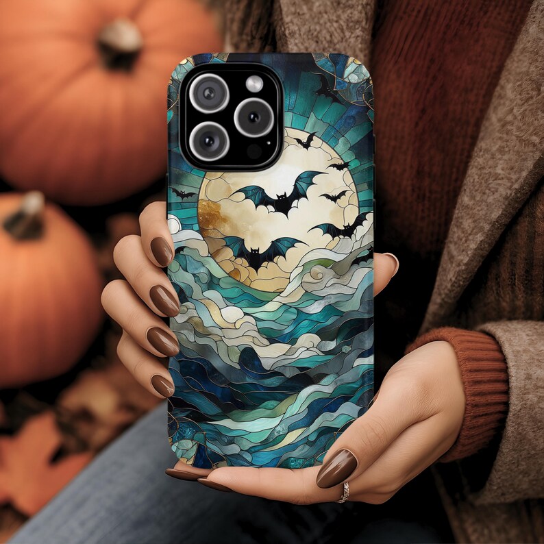 May include: A smartphone case featuring a Halloween design. The case displays a full moon with bats flying in front of it, set against a backdrop of blue and teal stained glass-style waves. The case has a black border and a camera cutout.